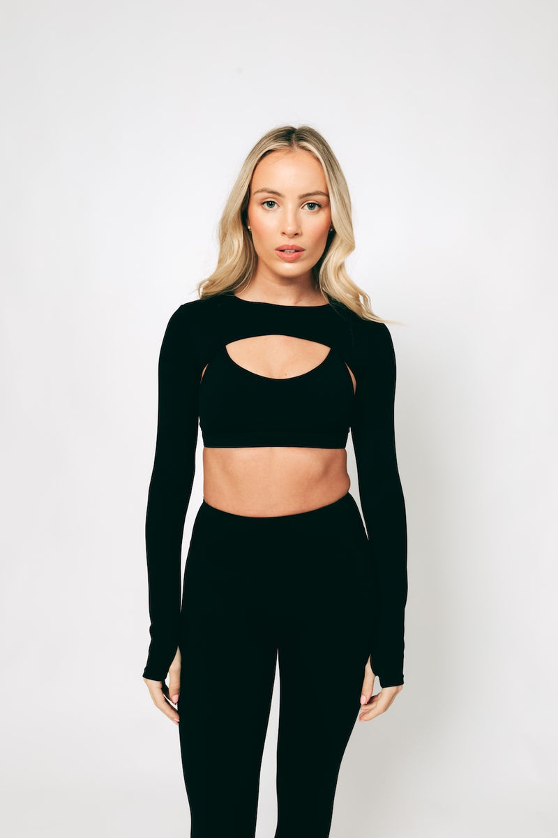 A model wearing a long-sleeved black crop top with a cut-out area at the front, made from buttery-soft, breathable fabric.