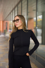 Woman wearing a black long-sleeve zip top from sosala and sunglasses outdoors.