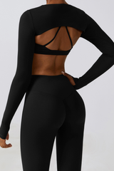 Person wearing a black long-sleeve crop top and leggings with open back design on a light gray background